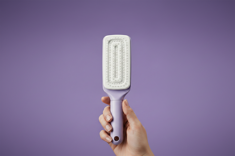 Hairbrush with collected hair on one side and a hand holding a purple  brush on the other, against a white and purple background.